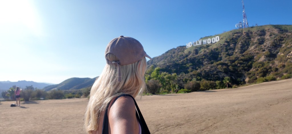 Woman in a cap looking up at the Hollywood Sign from a free hiking trail in Los Angeles