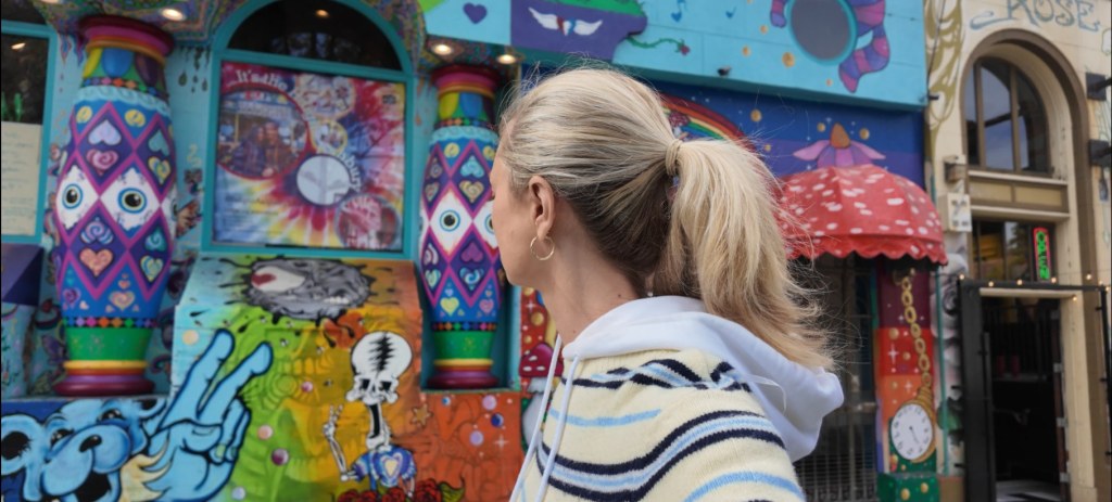 Woman with a blonde ponytail looking at a vibrant, colourful painted mural on a city street